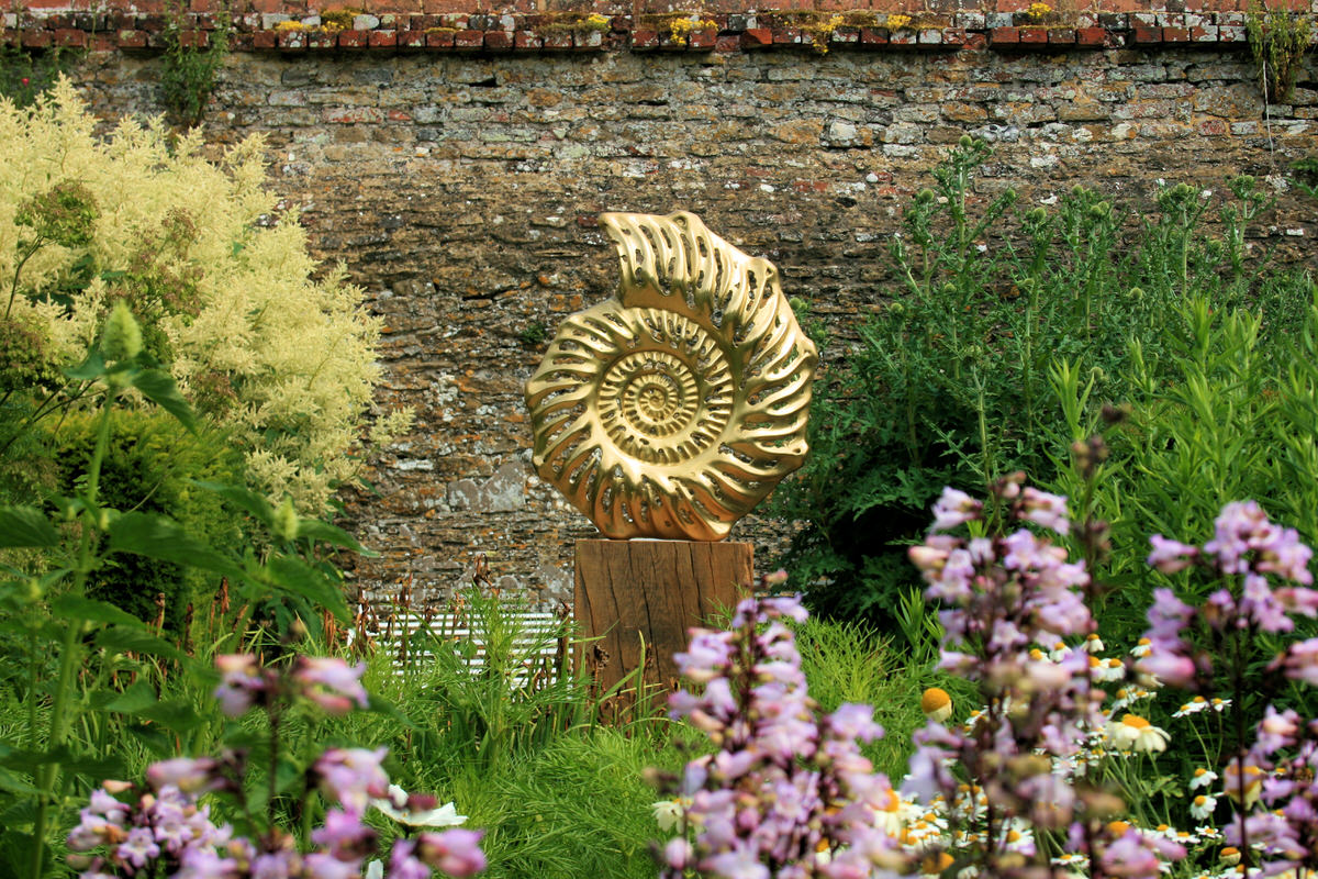 Ammonite slice outside bronze contemporary british sculpture in walled garden landscape by Mark Reed